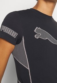 Svart träningsskorta av stretchmaterial. Har ett nätmönster, Puma-logotyp på ärmen och kontrasterande ljusgrå detaljer.