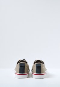 Zapatillas bajas de lona beige claro con tiradores negros y detalles rojos en suelas de goma blanca. Presentan un diseño duradero para el uso casual.