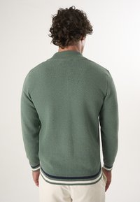 Suéter verde de punto con un acabado texturizado, cuello y puños acanalados, y rayas horizontales en azul marino y crema en el dobladillo.