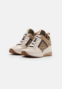 Witte en beige sneakers met een getextureerd bruine logopatroon, voorzien van gouden accenten en platte veters, tegen een neutrale achtergrond.