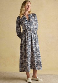 Pikad varrukad, tumesinine lillemusteriga kleit, millel on nööpidega kaelus, rõhutatud vöökoht ja voolav seelik. Kanda valgete mokassiinigadega.