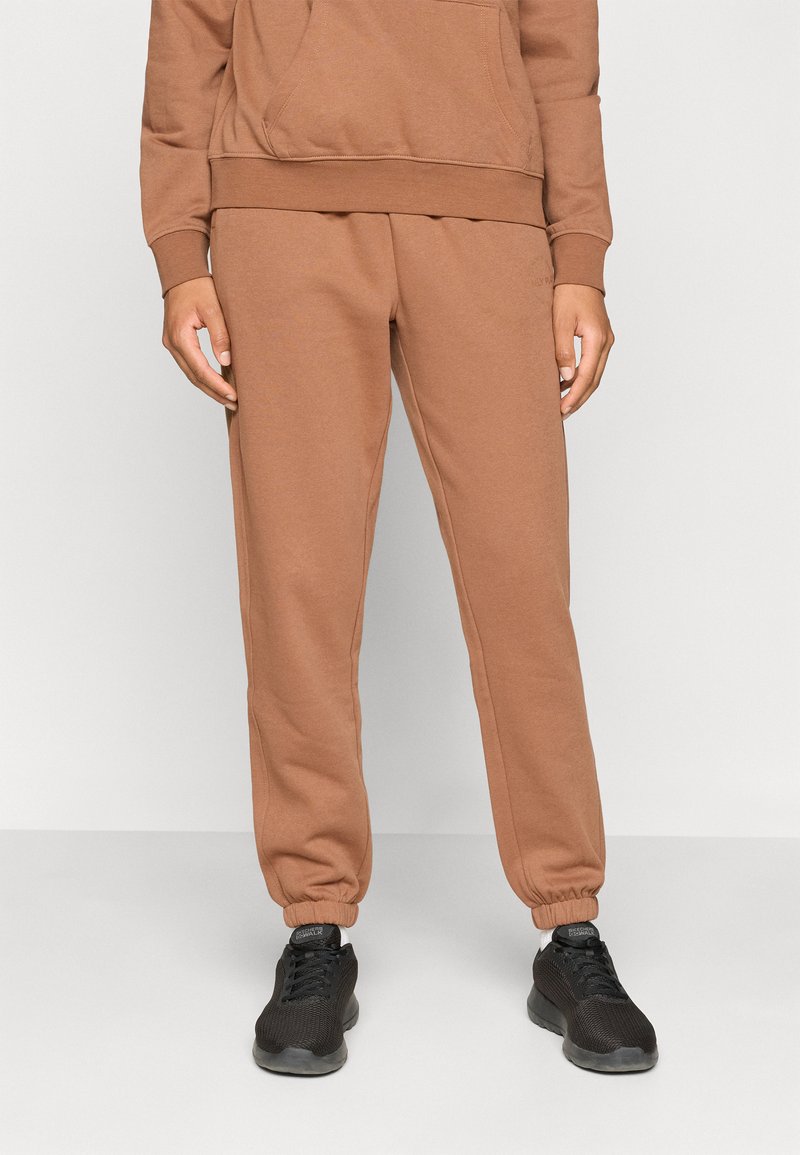 Brown sweatpants with elastic cuffs, featuring a smooth texture and relaxed fit. Paired with black athletic shoes for a casual look.