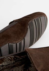 Mocassin en suède marron avec semelle en caoutchouc, doté d'une doublure texturée et d'une couture décorative le long du bord. Intérieur doux et confortable.
