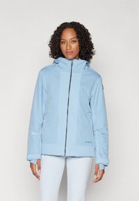 Vaaleansininen laskettelutakki, jossa vetoketjullinen suljenta, korkea kaulus ja kontrastisia teksturoituja paneeleja, joissa on logotyyppidetaljit hihaosassa.