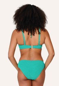 Tyrkysový bikini set s textúrovanou tkaninou, nastaviteľnými ramienkami a zapínaním na chrbte. Spodná časť s plným zakrytím a decentnými detailmi.
