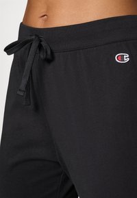Zwarte sweatpants met een trekkoord in de taille, zachte stof en een klein geborduurd logo aan de zijkant.