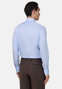 Jasnoniebieska koszula w paski z klasycznym kołnierzykiem, długimi rękawami i dopasowanym krojem, zestawiona z ciemnobrązowymi spodniami.