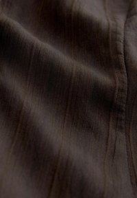 Tessuto marrone scuro con texture a costine verticali fini e pieghe morbide.