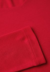 Nahaufnahme eines roten Baumwollstoffs mit glatter Textur. Das Bild zeigt einen gefalteten Ärmel mit sichtbaren Nähdetails.