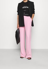 Blazer negro sobre una camiseta gráfica negra, combinado con pantalones amplios rosa claro y sosteniendo un bolso negro.