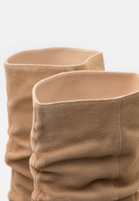 Bottines en daim beige au design décontracté, avec une surface texturée, des bords bruts et un dessus ouvert.