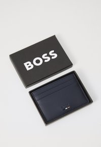 Navy leather cardholder with multiple card slots, embossed logo, and minimalistic design, presented in a black branded box.