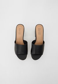 Black vegan slide sandals with a wide, smooth upper band and a low heel. Textured interior with a neutral sole.
