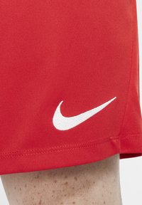 Pantalones cortos deportivos rojos hechos de una tela suave, con un logo de Nike bordado en blanco en el lado izquierdo cerca del dobladillo.