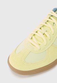 Limegul sneaker med en blanding av semsket skinn og glatt stoff, rund tå, matchende lisser og en brun gummisåle med teksturert mønster.