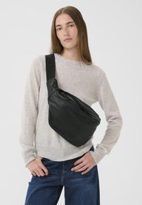 Borsa a tracolla in pelle nera con finitura lucida, dotata di un unico scomparto con zip e di una tracolla in nylon regolabile.