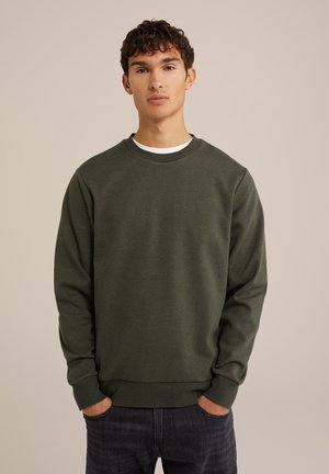 Donkergroene sweatshirt van textuurstof, met een ronde hals, lange mouwen en ribgebreide boorden en onderkant, gecombineerd met donkerblauwe jeans.