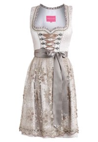 Tenue traditionnelle avec un corsage blanc à lacets sur le devant, une jupe beige brodée et un nœud en satin à la taille. La jupe est ornée de motifs floraux.