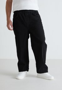 Pantalones de algodón negros sueltos con un acabado texturizado, con cintura elástica y bolsillos laterales, combinados con zapatillas blancas.