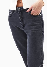 Jeans oscuros de mezclilla, con un corte ajustado, diseño de cinco bolsillos y costura visible. La tela tiene una textura suave.