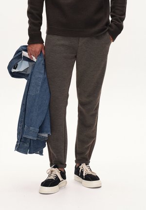 Gray sweatpants in a soft, textured fabric with tapered legs and side accents. A denim jacket is held in one hand, paired with black sneakers.
