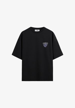 T-shirt nera a maniche corte con collo rotondo e piccolo serpente viola con grafica e testo nella zona sinistra del petto.