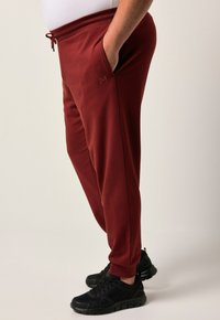 Bordeaux joggers van zacht materiaal, voorzien van zijzakken en een geribde tailleband. Gecombineerd met zwarte sportschoenen, die textuur materialen tonen.