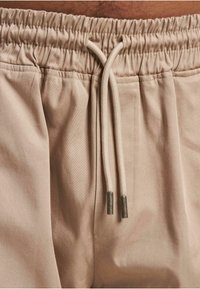 Șorturi bej cu șnur, dotate cu un talie elastică, având o textură netedă și șnururi cu vârfuri din metal. Design curat și minimalist.