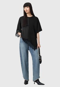 Sort top med blondekanter, løs pasform og korte ærmer, parret med højtaljede, vide blå denimjeans og spidse sorte støvler.