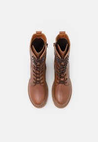Hnědé kožené šněrovací boty s kulatou špičkou, silnou podrážkou a kovovými akcenty. Obsahují zip a texturovanou podšívku.