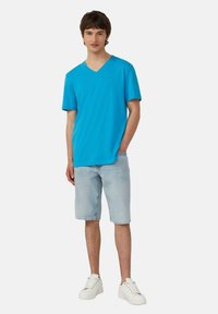 T-shirt blu a V in cotone, abbinata a pantaloni corti di jeans chiari e scarpe da ginnastica bianche. Design semplice con maniche corte e vestibilità comoda.