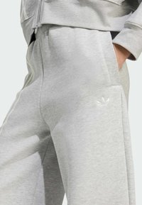 Joggers de poliéster gris con piernas ajustadas, cinturilla elástica, bolsillos laterales y un sutil logo bordado en el muslo izquierdo.