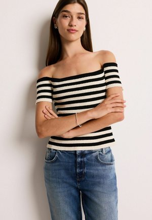 Off-shoulder gestreepte top in zwart en crèmekleurige ribstof, met korte mouwen. Gecombineerd met blauwe denim jeans met klassieke zakken.