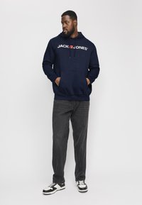 Felpa con cappuccio blu navy con logo bianco, dotata di tasca a marsupio. Abbinata a jeans grigi e sneaker in bianco e nero.