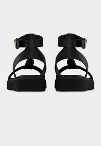 Μαύρα πλατφόρμα σανδάλια με λουράκι στον αστράγαλο, κατασκευασμένα από λείο υλικό. Διαθέτουν μινιμαλιστικό σχεδιασμό και υφή στη μαύρη σόλα με αυλακώσεις.