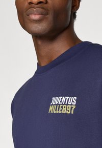 T-shirt de algodão azul marinho com decote redondo e uma estampa gráfica que diz "JUVENTUS MILLE897" em texto branco e amarelo.