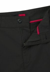 Pantalons noirs avec une fermeture à glissière et un bouton. Dotés d'une accentuation rouge à la taille et d'une texture de tissu lisse et durable.