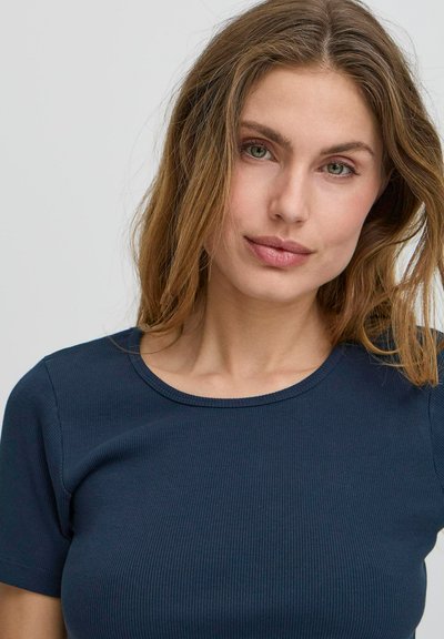 Cămașă scurtă cu mânecă, de culoare albastru închis, cu guler rotund. Țesătura are o textură netedă, prezentând un design ajustat care evidențiază silueta.