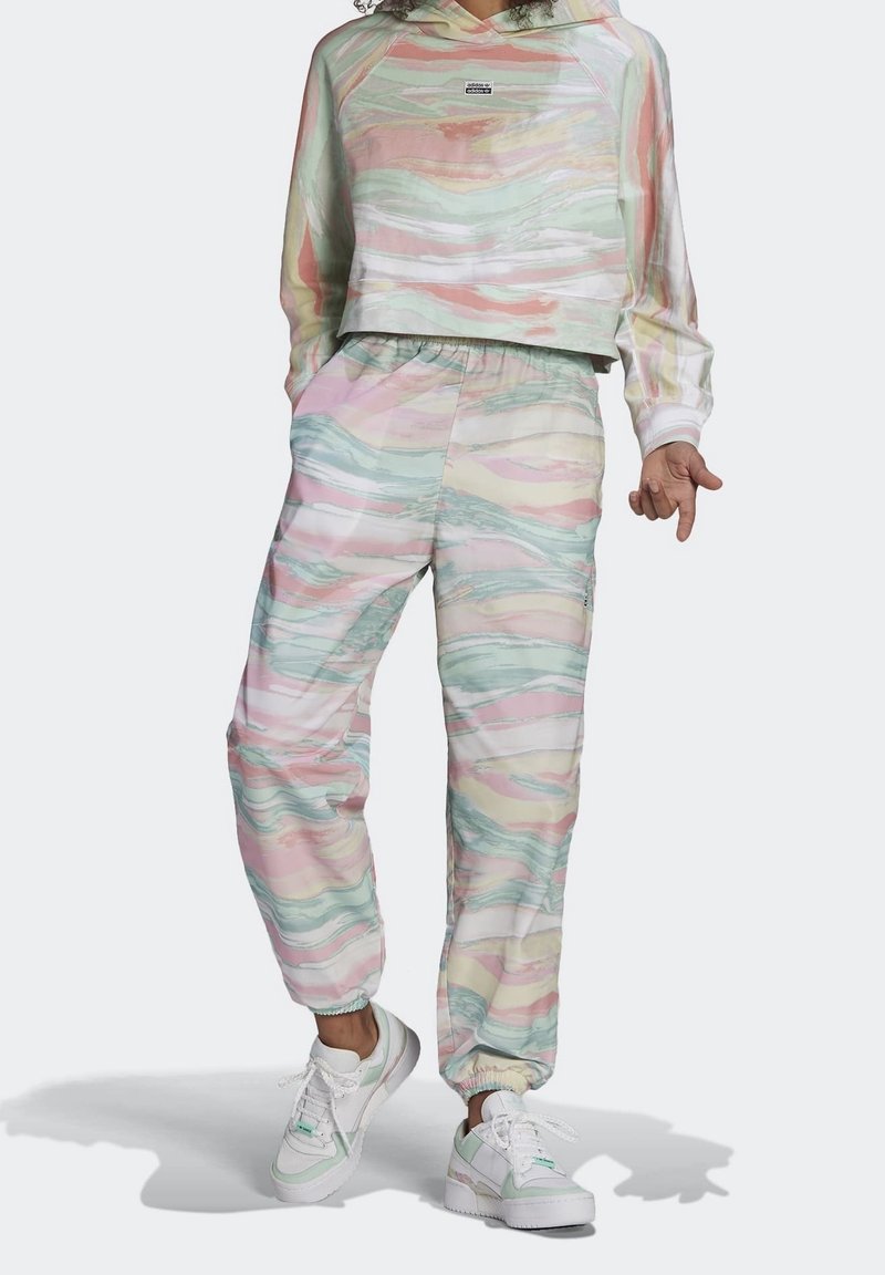 Persona che indossa una felpa con cappuccio a motivo a spirale pastello e pantaloni jogger abbinati, con sneakers bianche e verde menta.