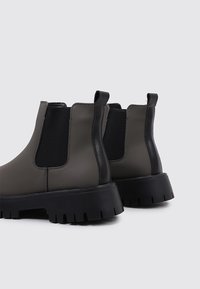 Botines de cuero sintético gris con paneles elásticos negros y suelas gruesas de goma negra, con lengüetas para facilitar su uso.