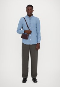 Ljusblå skjorta med knappar, grå byxor och svarta skor. Brun crossbody-väska. Slät tygkvalitet, skräddarsydd passform, en bröstficka.