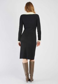 Czarna sukienka z prążkowanej tkaniny z kremowym kołnierzem i mankietami, dopasowany krój, do kolan, w zestawie z beżowymi botkami do kolan.