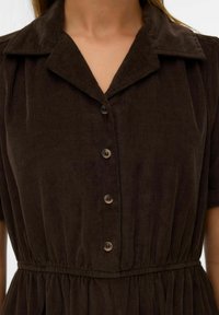 Robe en velours côtelé marron avec un devant boutonné, des manches courtes et une taille cintrée. Remarquable pour sa texture côtelée et son design de col classique.