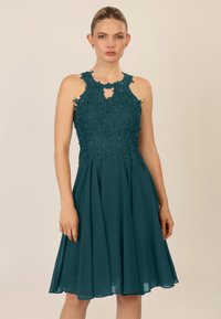 Teal knielang jurkje met een bloemenkant lijfje, halterhals en een keyhole-detail. De vloeiende chiffon rok verbetert de beweging.