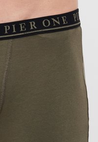Olivgrüne Boxershort mit einem schwarzen Bund, auf dem "PIER ONE" in goldenen Buchstaben steht. Der Stoff ist glatt und elastisch mit einem schlichten Design.