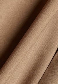 Gros plan d’un tissu brun clair lisse, tissé serré, avec de doux plis diagonaux et des variations subtiles de texture.