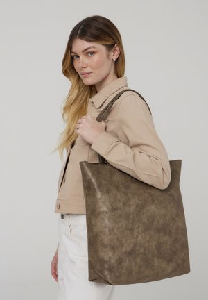Borsa tote in finta pelle marrone con una superficie liscia e bordi morbidi, dotata di manici doppi e un design spazioso. Il modello posa con la borsa sulle spalle.