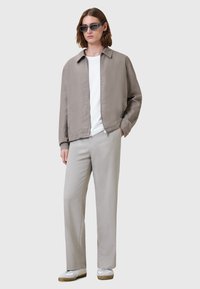Giacca leggera grigia con colletto, t-shirt bianca sotto, pantaloni grigi chiari e sneakers bianche, esposti su uno sfondo neutro.