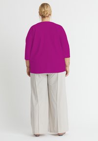 Fuchsia 3/4-Ärmel-Bluse mit geradem Schnitt, kombiniert mit weit geschnittenen cremefarbenen Hosen. Glatte Textur; keine auffälligen Muster oder Akzente.