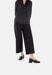 Camicia nera in satin con bottoni e orlo curvo, abbinata a pantaloni neri a gamba ampia. Completata con mocassini neri con tacco basso.